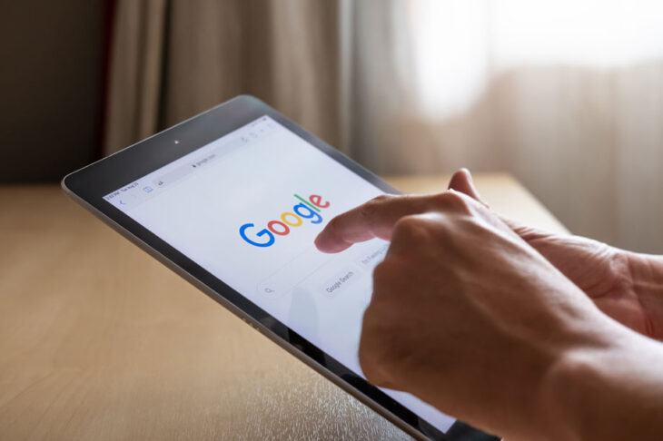 A close up shot of a pair of hands holding an electronic tablet, the google logo is visible on screen