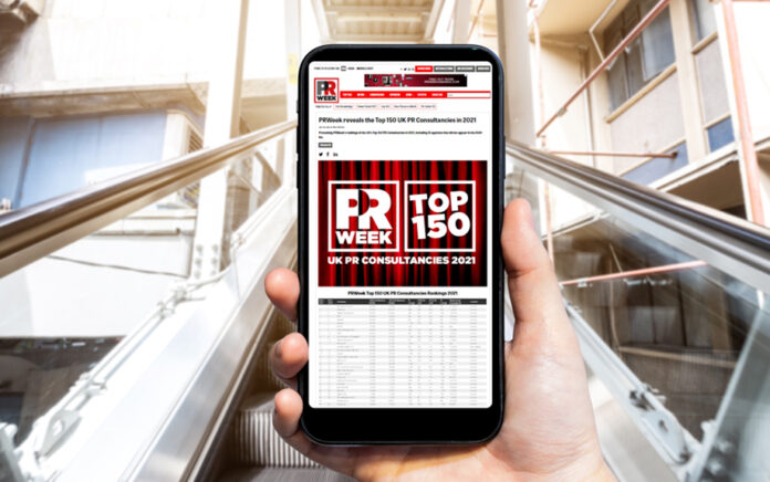 A close up shot of a mobile phone being held up in front of an escalator, with a news article on screen